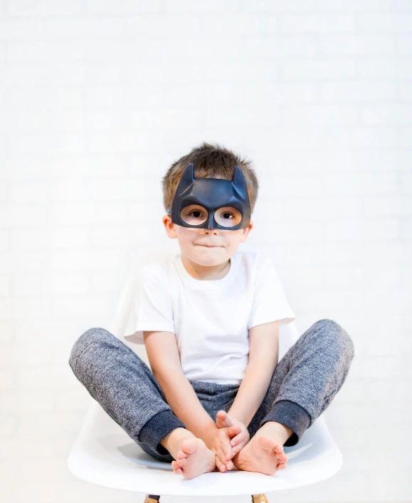 a young boy sitting on top of a white chair, by Ellen Gallagher, pexels, super hero mask, ryan renolds as batman, full product shot, small