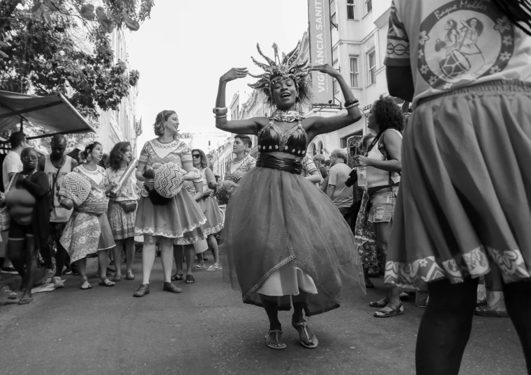 a group of people that are standing in the street, a black and white photo, by Ingrida Kadaka, pexels contest winner, figuration libre, carnival on the background, she is dancing. realistic, african princess, san francisco