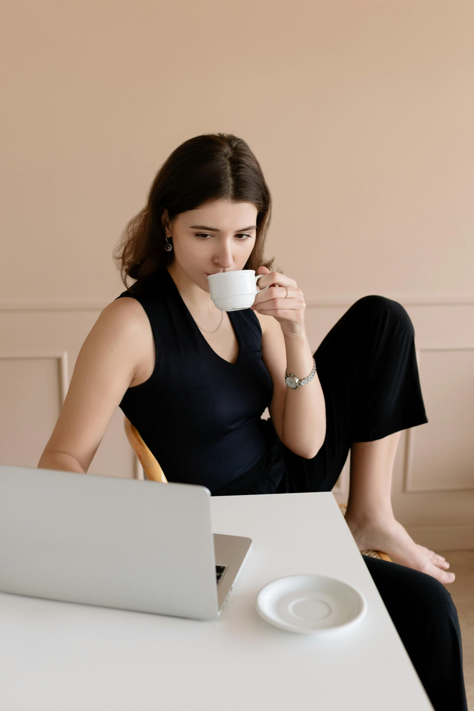 a woman sitting at a table with a laptop and a cup of coffee, wearing black camisole outfit, curated collections, slender woman, profile image