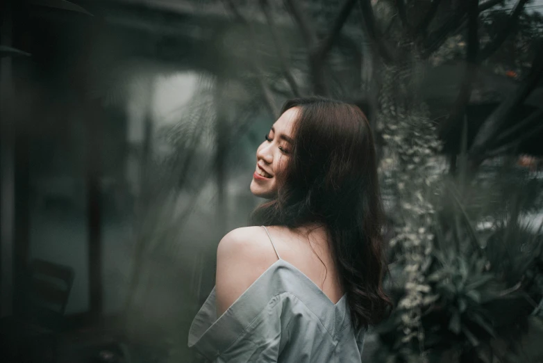 a woman that is standing in the grass, a picture, pexels contest winner, smiling :: attractive, haze over the shoulder shot, asian woman, on a gray background