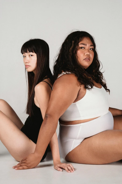 a couple of women sitting next to each other, an album cover, inspired by Wang Duo, unsplash, strong fat bacchanalian body, wearing leotard, asian descent, white and black