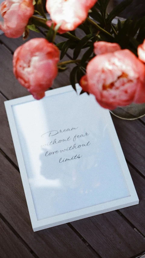 a book sitting on top of a wooden table, a poster, inspired by Khalil Gibran, unsplash, peonies, white frame, dream like, hand drawn type