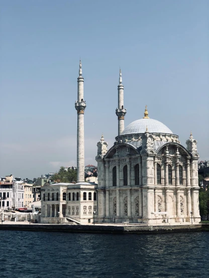 a large white building sitting on top of a body of water, inspired by Osman Hamdi Bey, pexels contest winner, hurufiyya, black domes and spires, marbled columns, viewed from the harbor, brown
