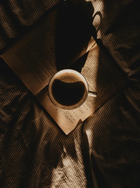 a book sitting on top of a bed next to a cup of coffee, inspired by Elsa Bleda, pexels contest winner, dark angel of coffee, gif, 15081959 21121991 01012000 4k, sombre mood