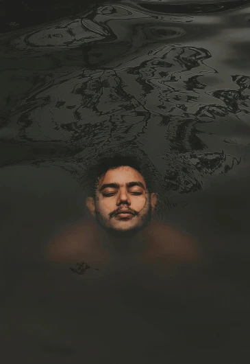 a man floating in the water with his eyes closed, an album cover, pexels contest winner, ariel perez, black oil bath, post malone, somber expression