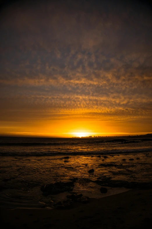 the sun is setting over the water at the beach, by Peter Churcher, yellow clouds, high quality image, landscape photo, afar