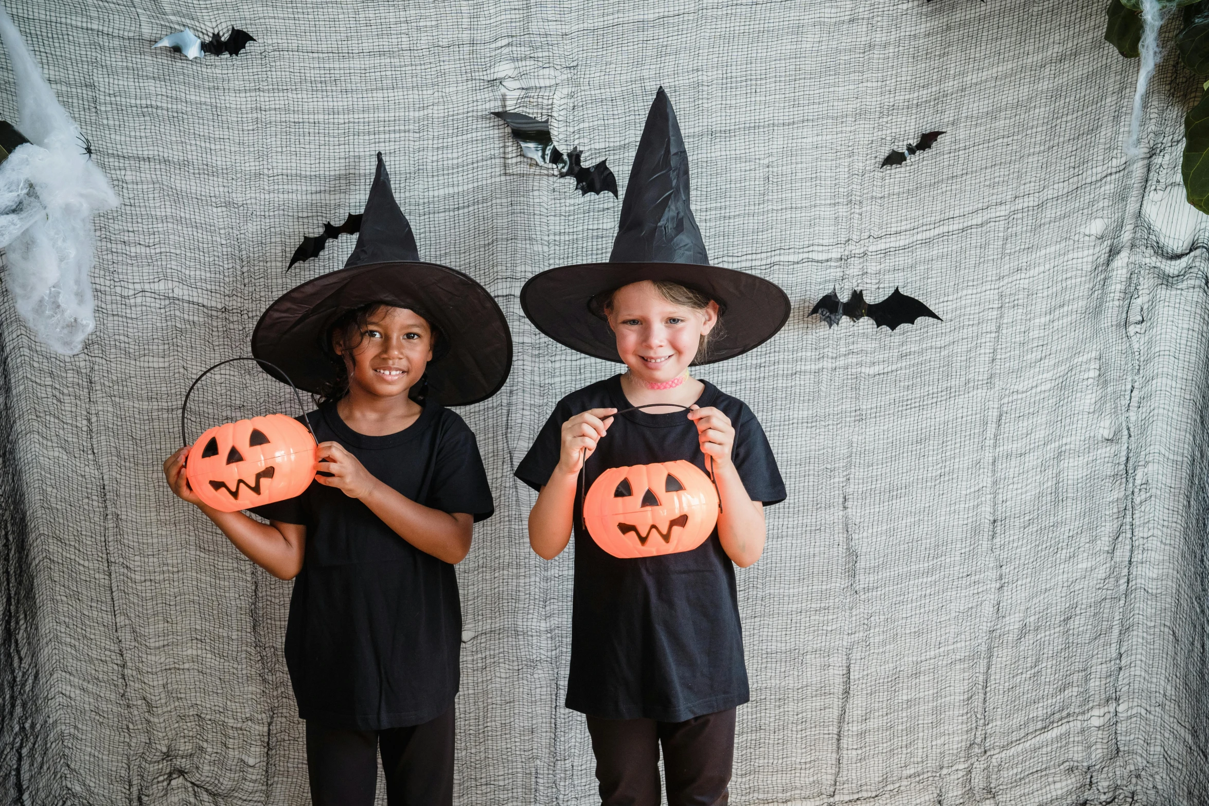 a couple of kids standing next to each other holding pumpkins, a cartoon, pexels, antipodeans, pointed black witch hat, square, indoor picture, no - text no - logo