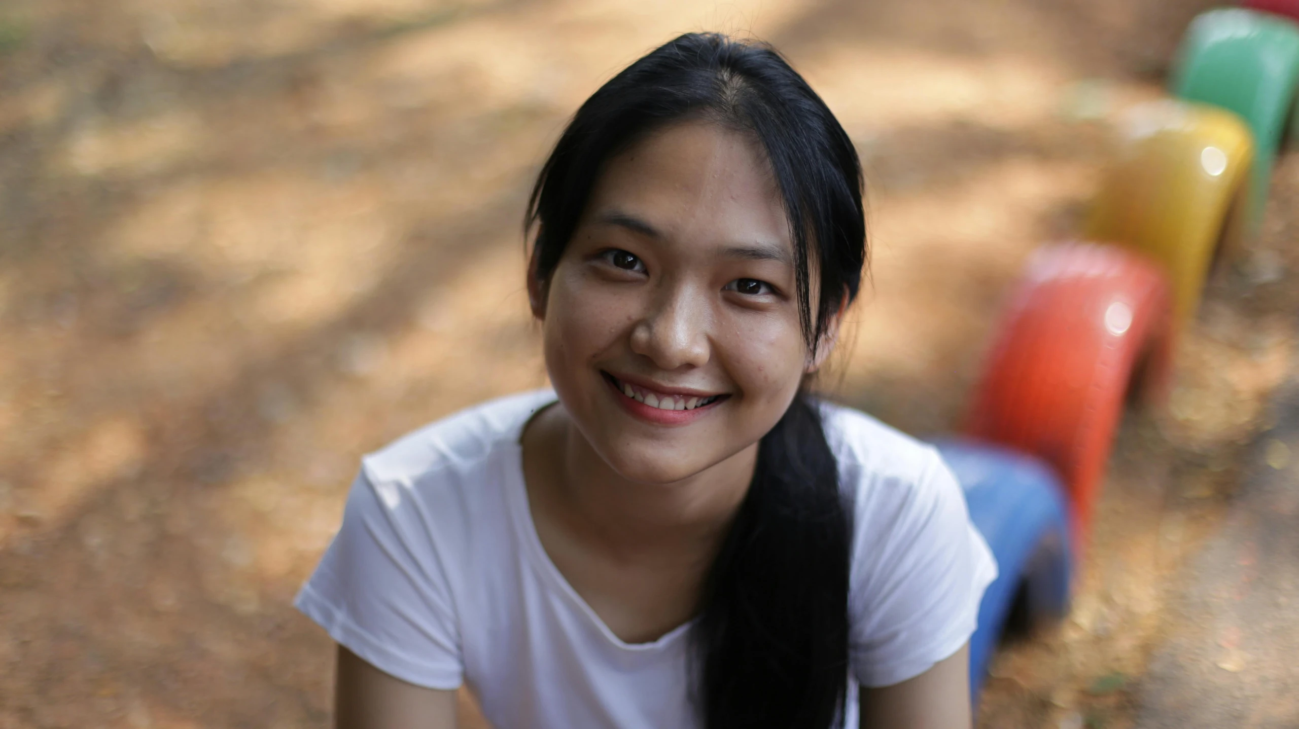 a woman with long black hair sitting on a bench, smiling into the camera, malaysian, portrait image, pictured from the shoulders up