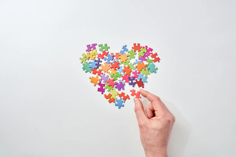 a person holding a piece of puzzle in the shape of a heart, a jigsaw puzzle, inspired by Myles Birket Foster, interactive art, multi - coloured, white bg, teaser, 1 6 x 1 6