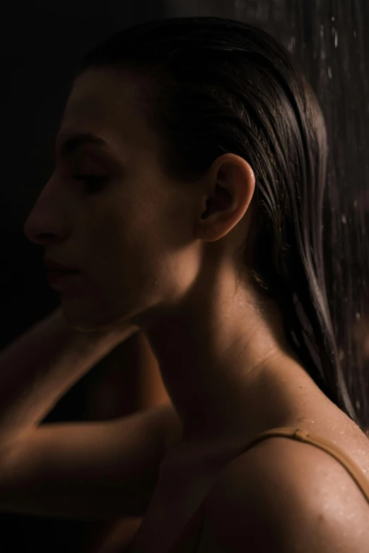 a woman standing in front of a shower head, inspired by Elsa Bleda, slicked-back hair, in a dark studio room, with textured hair and skin, a woman's profile