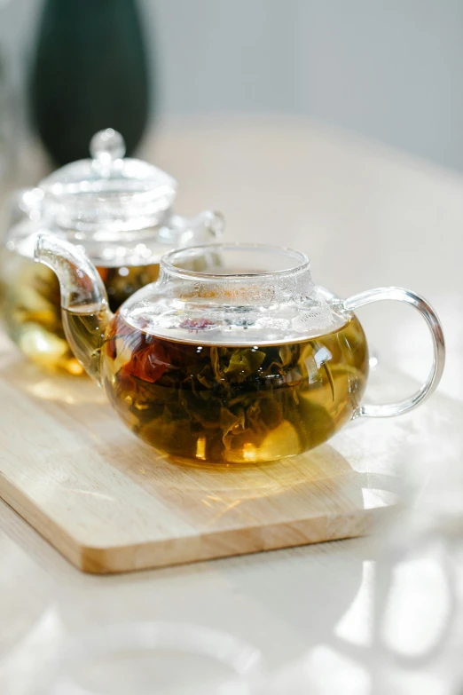 two cups of green tea sit on a cutting board, a still life, by Tan Ting-pho, pexels, teapot, translucent, square, banner