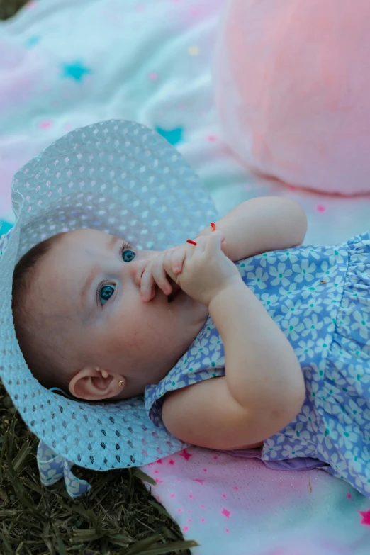 a baby laying on top of a blanket next to a pink ball, by Alice Mason, pexels contest winner, wearing wide sunhat, having a picnic, hand on her chin, pastel blue