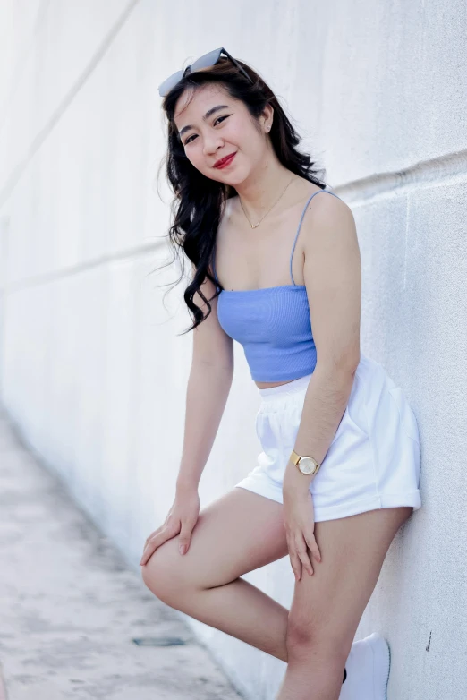 a woman in a blue top and white shorts leaning against a wall, inspired by Ina Wong, pexels contest winner, wearing a cropped tops, relaxing and smiling at camera, avatar image, sakimichan