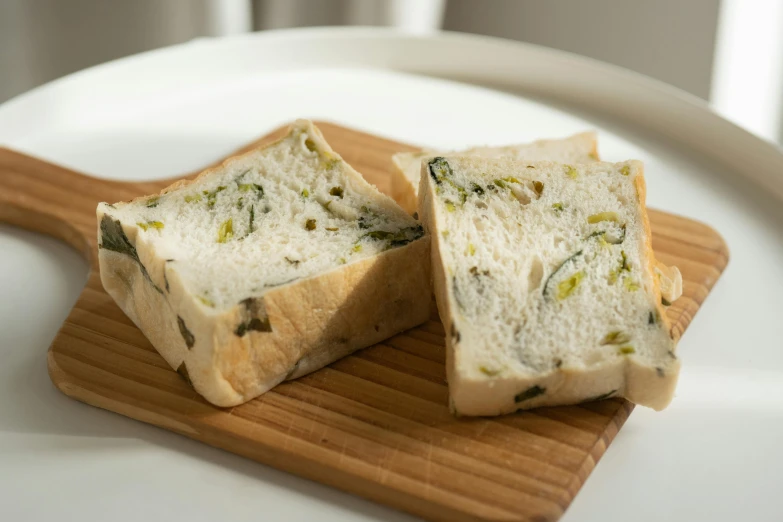 a piece of bread sitting on top of a wooden cutting board, inspired by Maki Haku, unsplash, mingei, olives, chiffon, square, green