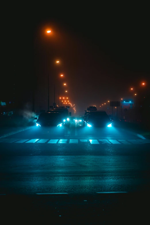 a group of cars driving down a street at night, an album cover, inspired by Elsa Bleda, pexels contest winner, cyan fog, intersection, cyberpunk photo, volumetric fog light