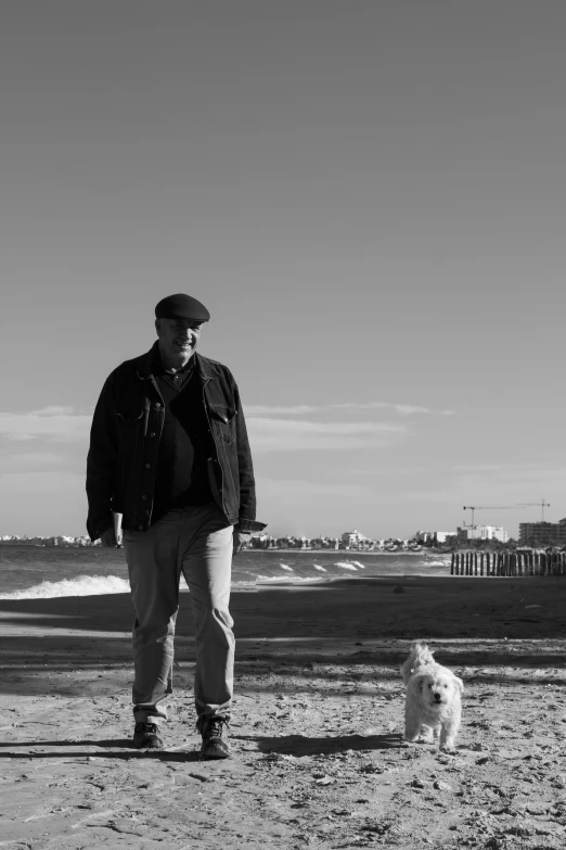 a man standing on top of a sandy beach next to a white dog, a black and white photo, inspired by Max Dupain, portrait!!!, - n 5, in the city, senor salme