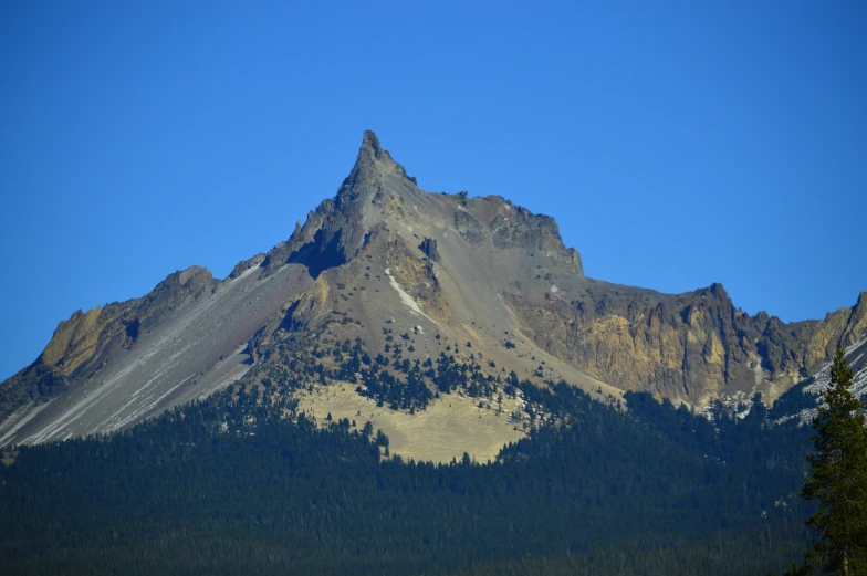 a mountain with a few trees in front of it, chiseled jaw, clear blue skies, british columbia, spire