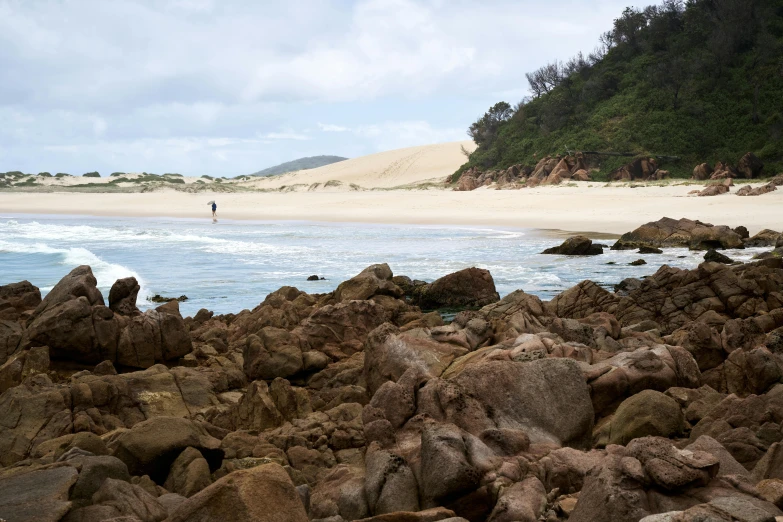 a man standing on top of a rocky beach next to the ocean, victorian arcs of sand, straya, sparsely populated, craig mulins