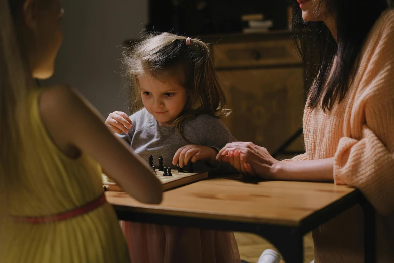 a woman and a little girl playing a game of chess, by Lee Loughridge, pexels contest winner, interactive art, on a table, six from little nightmares, cinematic footage, on wooden table