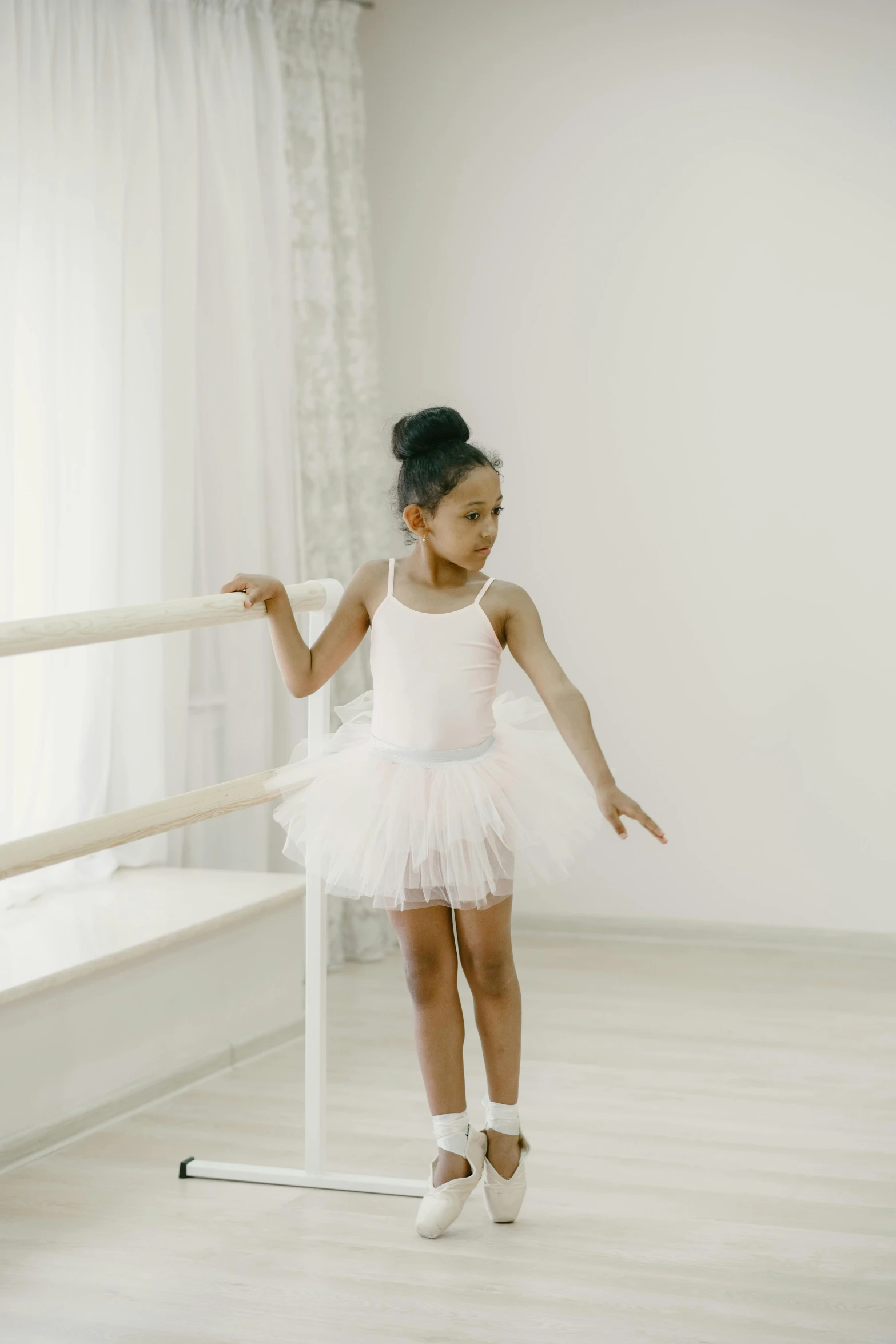 a little girl that is standing in a room, ballet pose, looking off to the side, all white, diverse