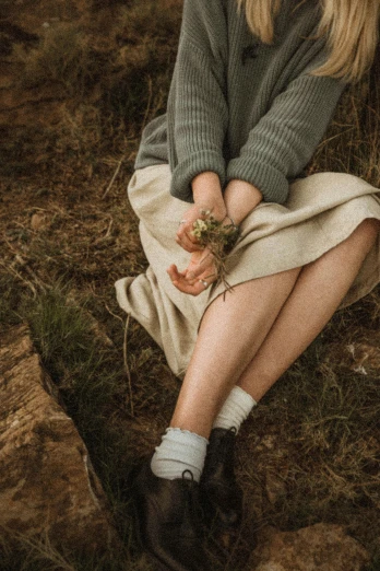 a woman sitting on the ground with a flower in her hand, trending on pexels, renaissance, roots and hay coat, cottagecore, small legs, muted colour