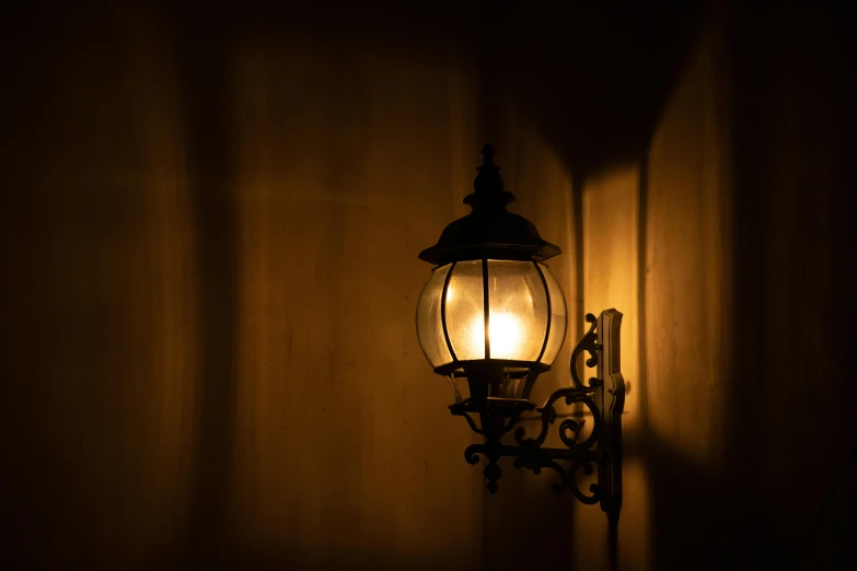 a light that is on the side of a wall, an album cover, inspired by Brassaï, pexels contest winner, lantern light, warm lantern lighting, gothic lighting, (night)