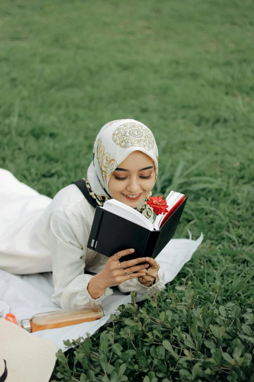 a woman laying in the grass reading a book, inspired by Maryam Hashemi, hurufiyya, religious, gif, college, malaysian