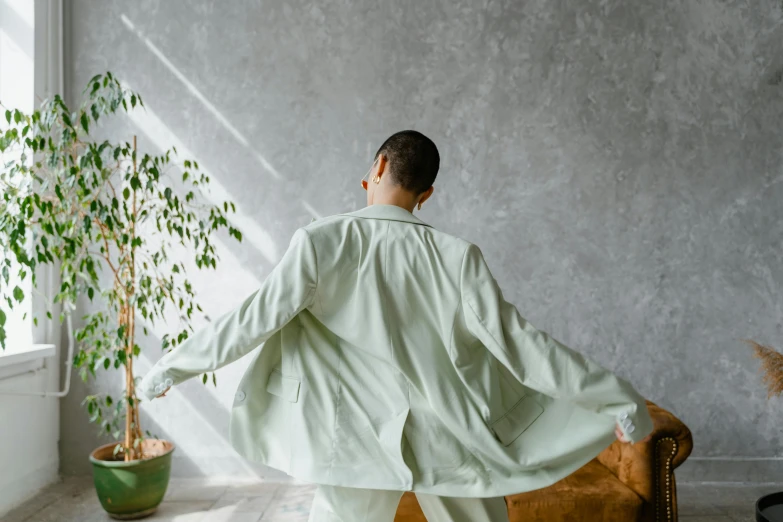 a man standing in a living room next to a potted plant, inspired by Fei Danxu, trending on pexels, green robes, back pose, labcoat, waking up