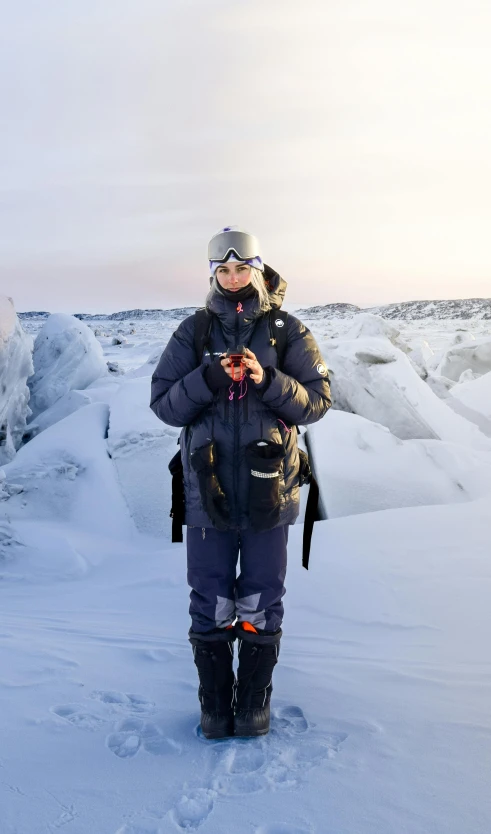 a person standing in the snow on a cell phone, a portrait, inspired by Nína Tryggvadóttir, pexels contest winner, mountains made out of icebergs, wearing adventuring gear, she is holding a smartphone, photographed for reuters