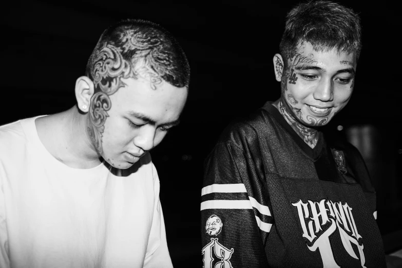 a couple of men standing next to each other, a black and white photo, by Basuki Abdullah, face tattoos, dj, at instagram, drip