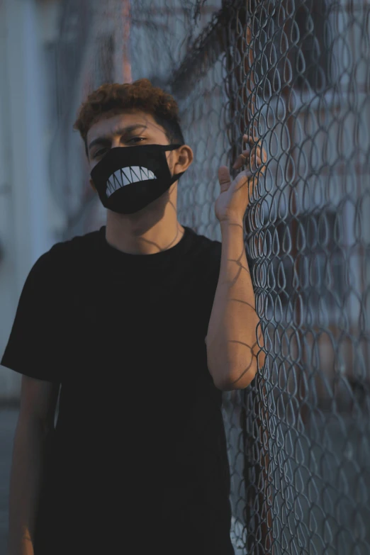 a man standing in front of a fence wearing a face mask, an album cover, pexels contest winner, glowing mouth, trending on r/streetwear, discord profile picture, profile picture 1024px