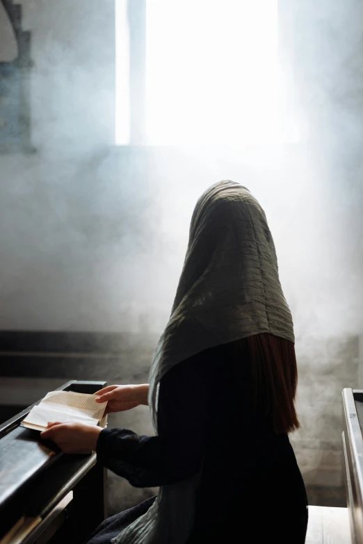 a woman sitting in a church reading a book, inspired by Modest Urgell, unilalianism, cloak covering face, smoky lighting, in a classroom, 2019 trending photo