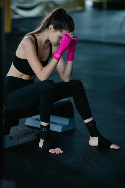a woman sitting on a bench in a gym, by Julian Allen, trending on pexels, renaissance, foot wraps, woman crying, hot pink and black, in a fighting pose