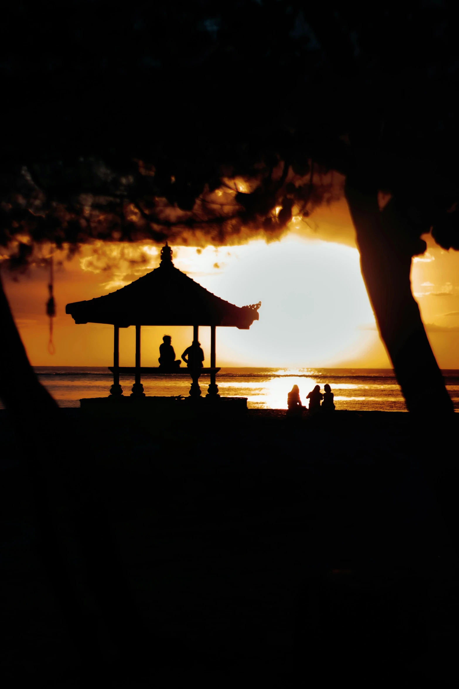 a group of people sitting on top of a sandy beach, during a sunset, gazebos, bali, f / 1 6