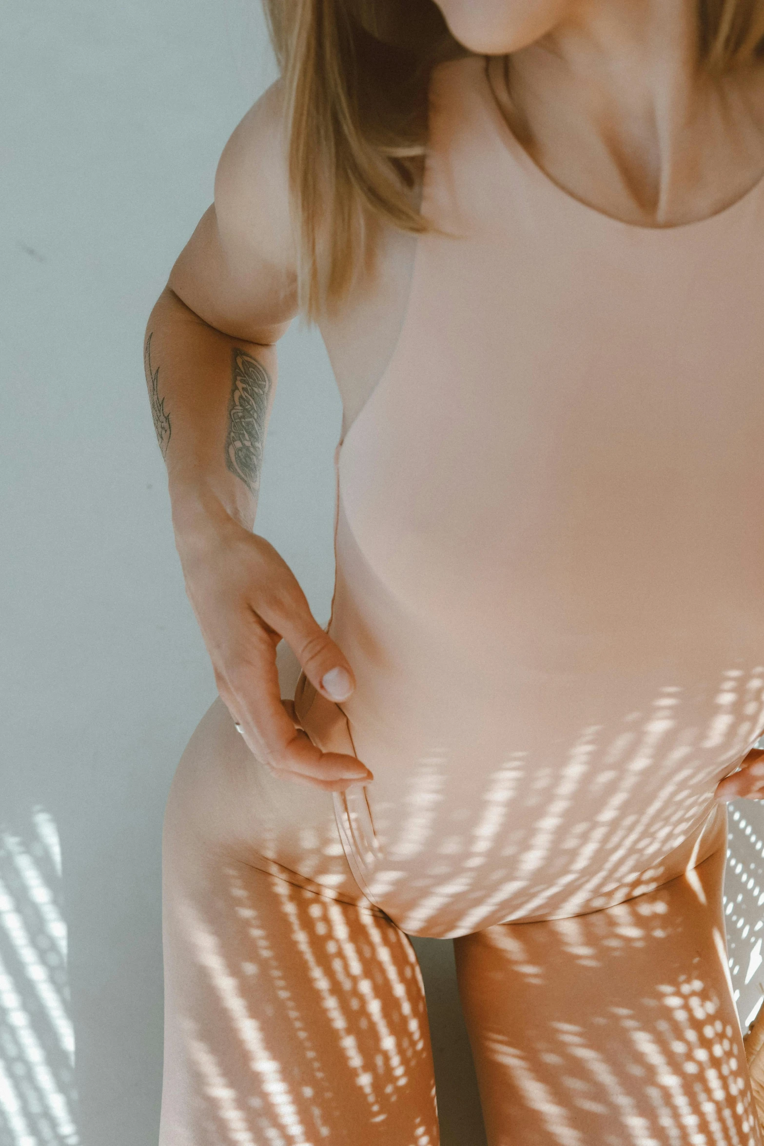 a woman standing in front of a white wall, inspired by Elsa Bleda, trending on pexels, light and space, pregnant belly, pink sunlight, muted colored bodysuit, skin detail