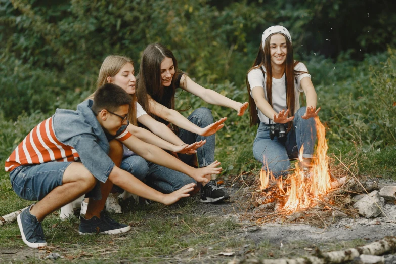 a group of young people sitting around a campfire, by Emma Andijewska, pexels contest winner, avatar image, teenager, holding a burning wood piece, promotional image