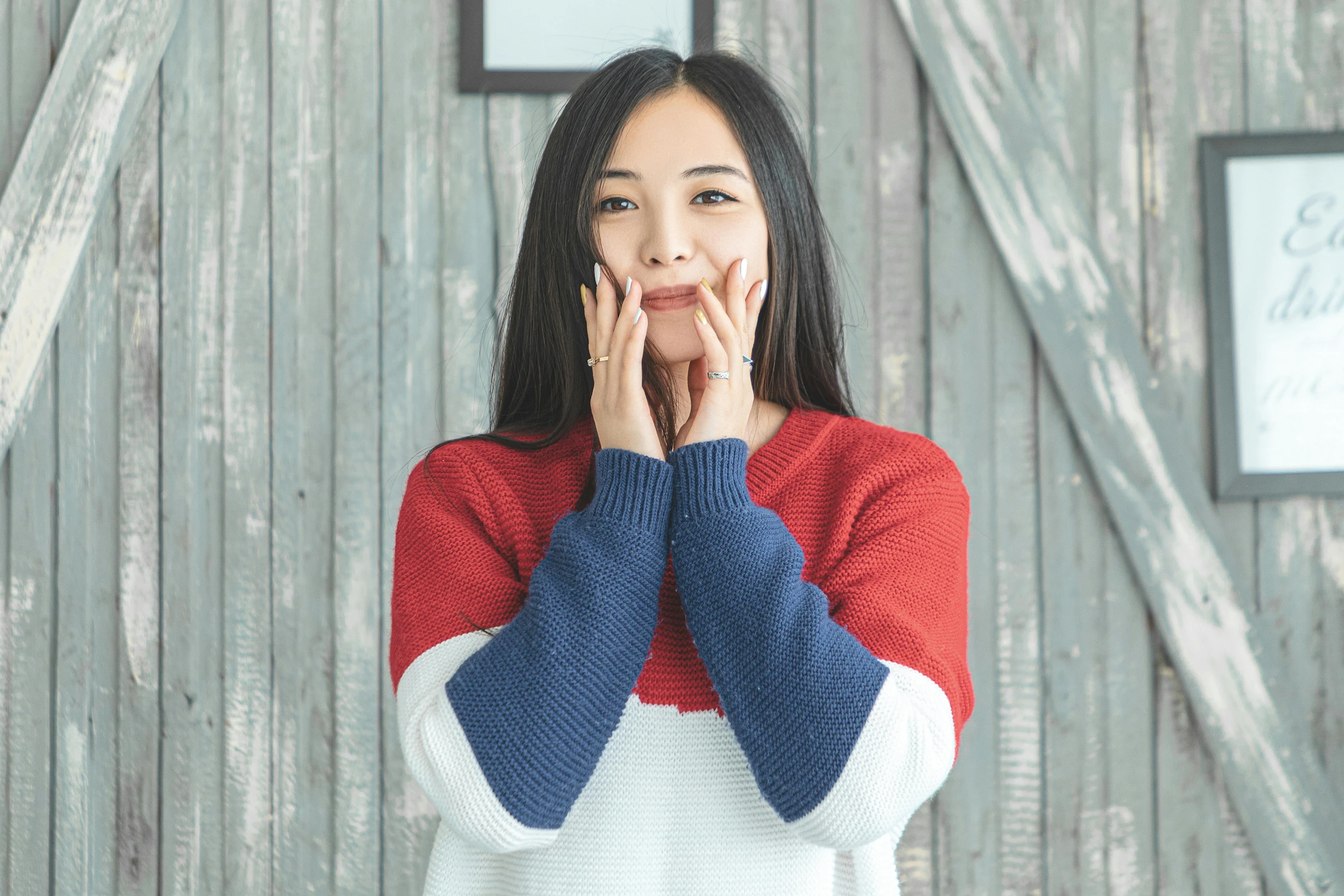 a woman standing in front of a wooden wall, inspired by Kim Jeong-hui, pexels contest winner, happening, wearing sweater, blue and red two - tone, korean woman, surprising