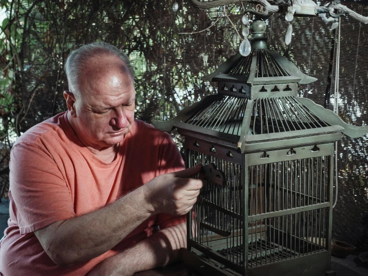 a man looking at a bird in a cage, portrait of hide the pain harold, gardening, shot with sony alpha, elias chatzoudis