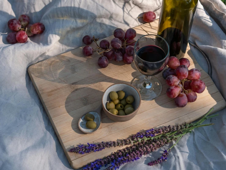 a bottle of wine sitting on top of a wooden cutting board, a still life, inspired by Ceferí Olivé, pexels contest winner, on a sumptuous tablecloth, grape, having a picnic, heath clifford