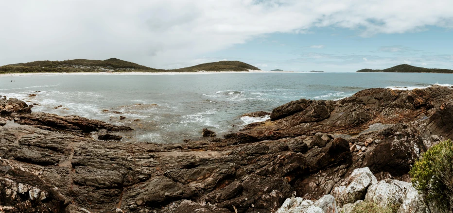 a man riding a surfboard on top of a rocky beach, panoramic photography, straya, whealan, landscape photo