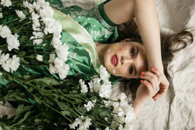 a woman laying on top of a bed covered in flowers, inspired by Elsa Bleda, trending on pexels, pre-raphaelitism, wearing green clothing, white flowers on the floor, green face, silk robes