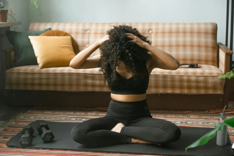 a woman sitting on a yoga mat in front of a couch, trending on pexels, hurufiyya, curls on top of his head, black, from the distance, thumbnail