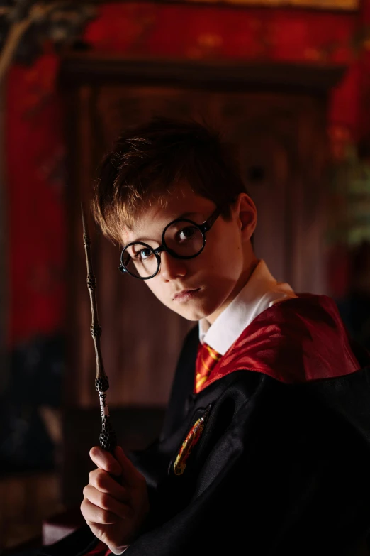 a young boy dressed as harry potter holding a wand, a portrait, pexels contest winner, man with glasses, ( ( theatrical ) ), hogwarts gryffindor common room, brown robes