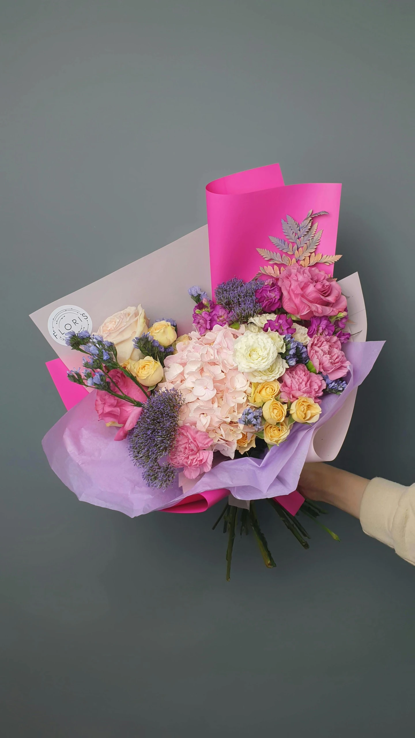 a person holding a bouquet of flowers in their hand, on a gray background, full of colours, (pink colors)