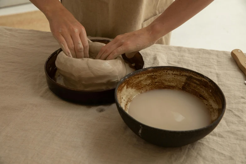 a person making a bowl of doughnuts on a table, a still life, inspired by Tani Bunchō, process art, ceramic base, brown, 4l, parchment