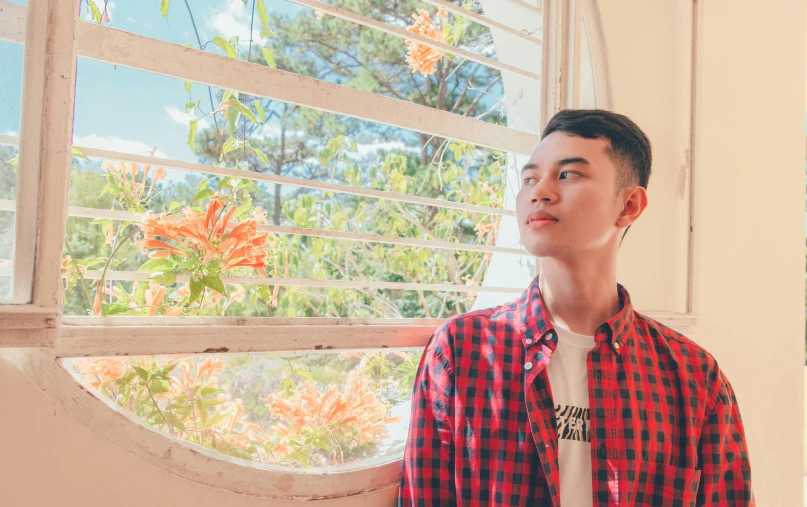 a young man standing in front of a window, inspired by Ryan Yee, pexels contest winner, light stubble with red shirt, mai anh tran, tommy 1 6 years old, on a bright day