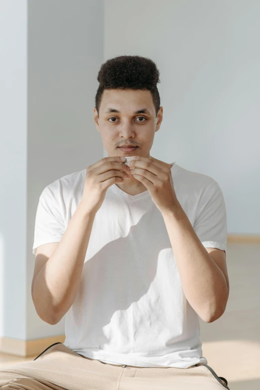 a man sitting on the floor eating a donut, pexels contest winner, clean shaven wide face, man standing in defensive pose, mixed race, dressed in a white t shirt