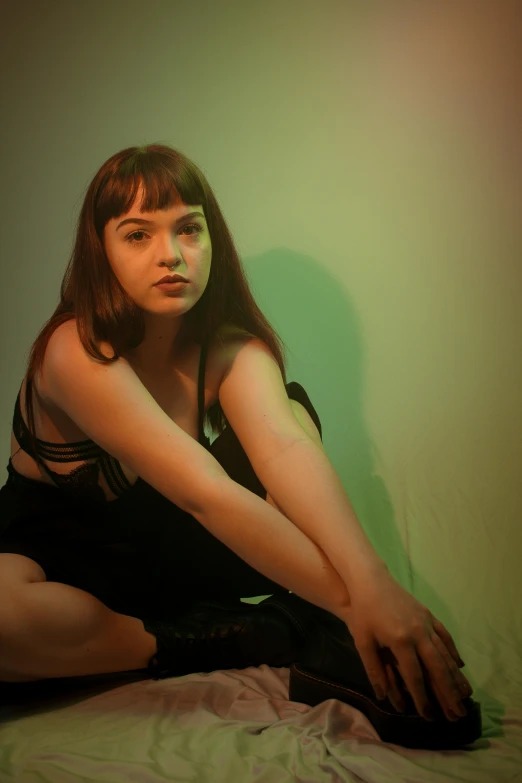 a woman sitting on top of a bed, an album cover, inspired by Nan Goldin, unsplash, renaissance, maisie williams, succubus in sundress portrait, green lights, she is wearing a black tank top