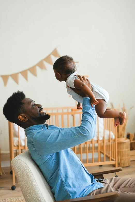 a man sitting in a chair holding a baby, pexels contest winner, symbolism, african canadian, raising an arm, hanging from the ceiling, caring fatherly wide forehead