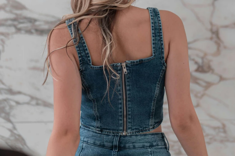 a woman standing in front of a marble wall, trending on pexels, croptop, double denim, corset, zippers